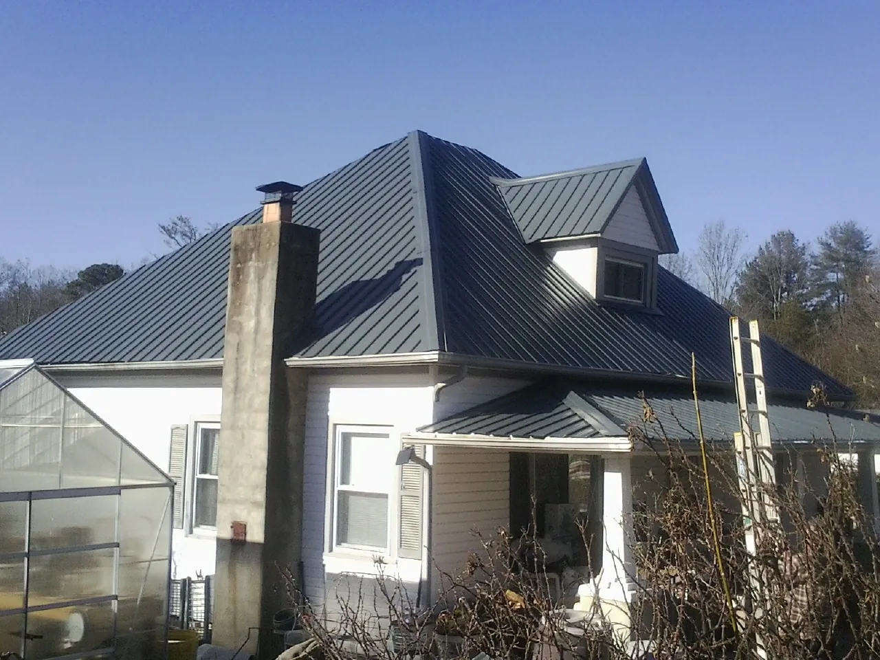 Dark blue standing seam metal roof on a white farmhouse with dormer — Slate & Tile Roof Repair by Roofing Brothers in Cerrillos