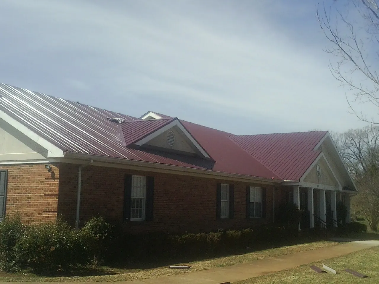 Red metal roof with gabled entries on a long brick building, from a Hail Damage Roof Repair job in Cerrillos