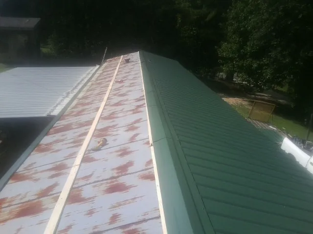 Old rusted panels beside newly installed green metal roofing — Wind Damage Roof Repair by Roofing Brothers in Cerrillos
