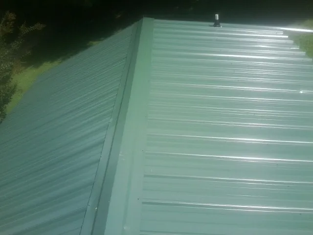 New green metal panels meeting at the ridge of a roof — Flat Roof Repair work by our crew in Cerrillos