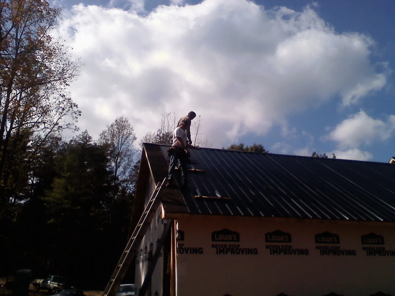 Roofer fastening dark metal panels high against a cloudy sky, from a Roof Inspection job in Cerrillos