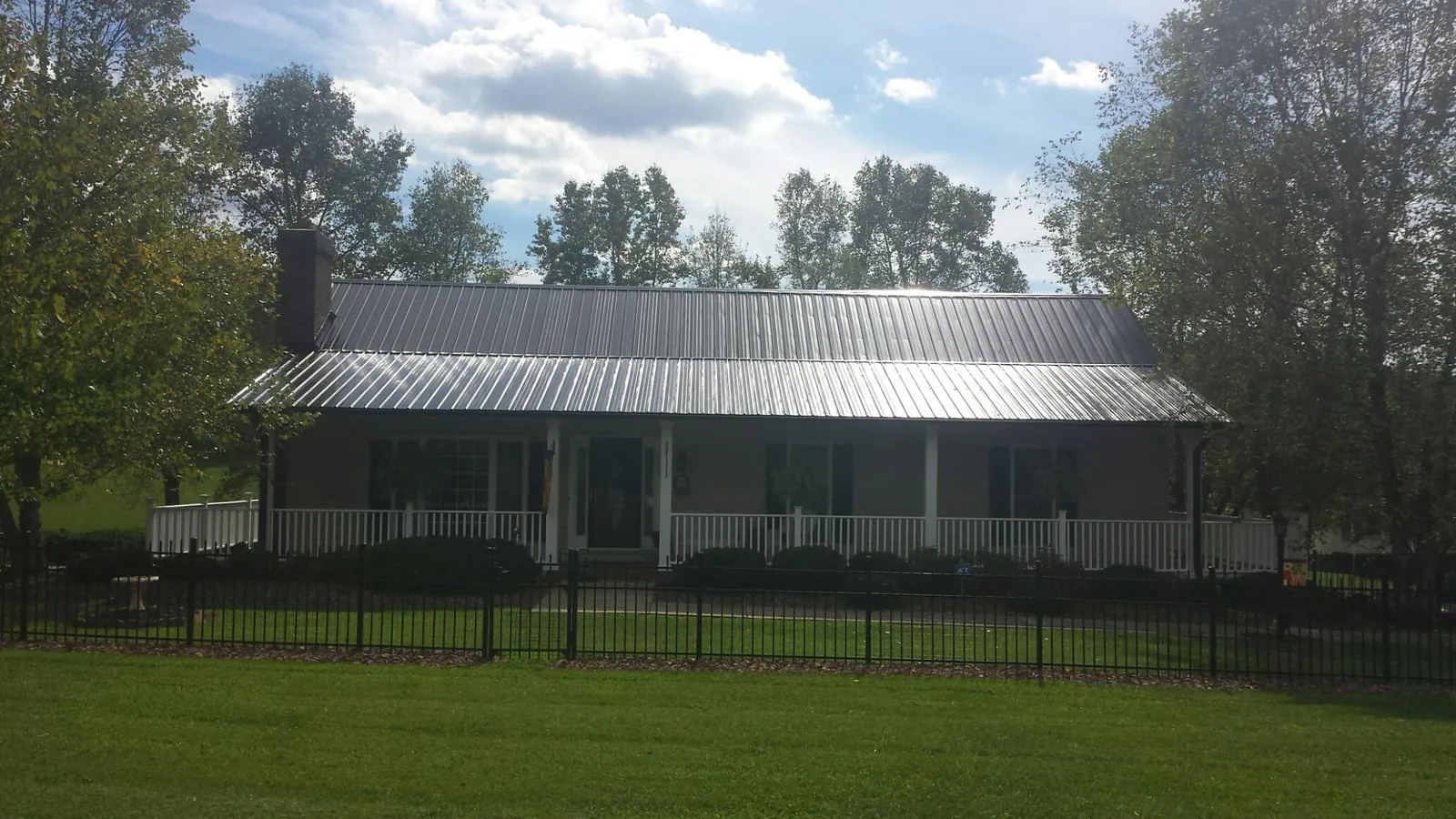 Gray metal roof on a brick ranch with a full width front porch — Gutter Guard Installation work by our crew in Cerrillos