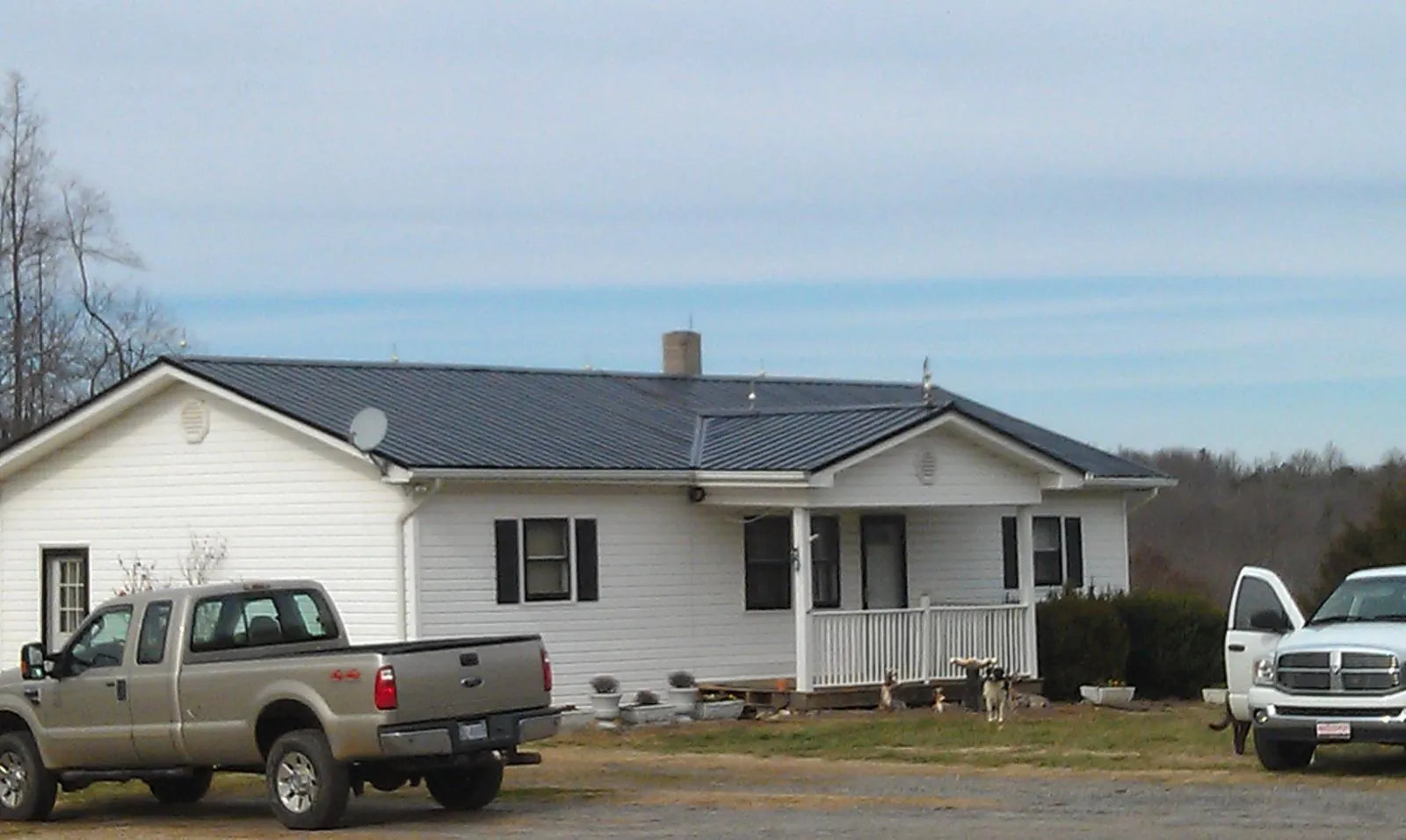 Finished dark metal roof on a white ranch home with work trucks parked in Cerrillos