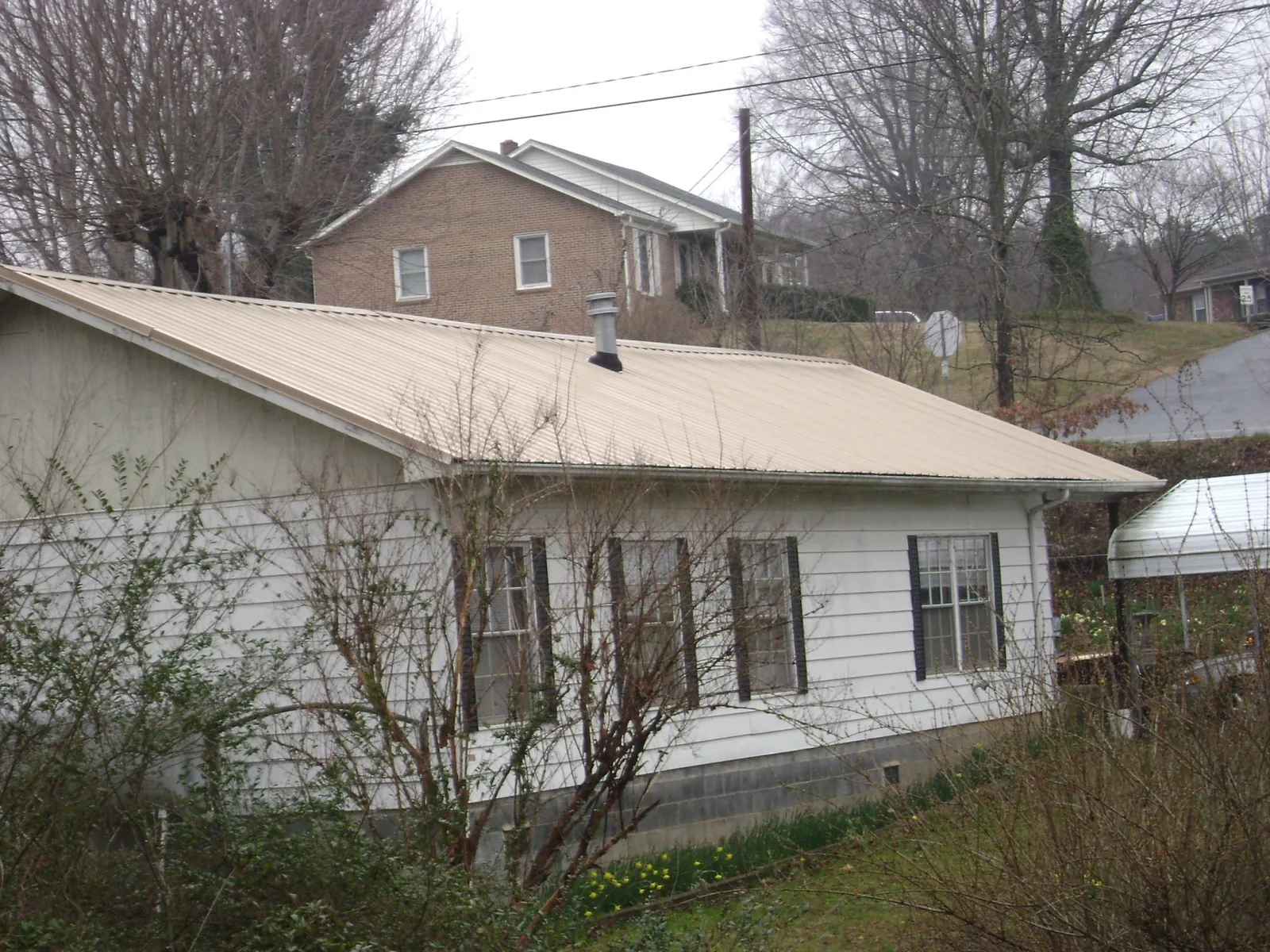 Tan metal roof on a white sided house set into a hillside — Commercial Roofing by Roofing Brothers in Cerrillos