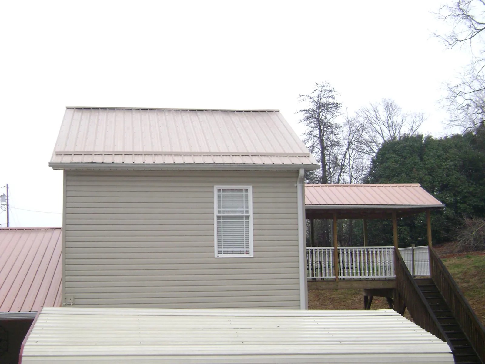 Tan metal roofs on a two story addition and attached porch, from a Roof Replacement job in Cerrillos